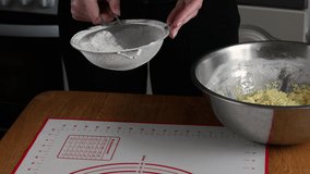 Close up of two pairs of female hands holding an iron sieve and sifting flour on a table with a pastry rug. High quality 4k footage