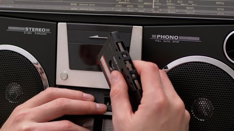 Fingers Men Inserted Audiocassette it in Tape Recorder, Pressed Play Button. Old cassette with magnetic tape, 90s. Vintage audio player with indicators and two speakers. Zoom. Slow-motion. Close-up