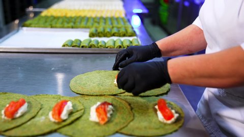 Chef in black gloves preparing pancakes with stuffing. Green crepes are rolled with fish and cheese inside. Close up.