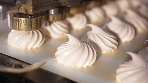 White creamy marshmallows are squeezed on the moving conveyor belt. Close up. Automated line for sweet products manufacturing. Confectionery concept.
