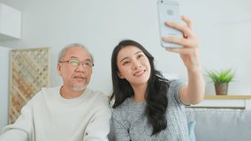 Asian lovely family, daughter use phone video call with senior father. Young beautiful girl and elderly older male sit on sofa enjoy communicate by internet online talk together in living room at home