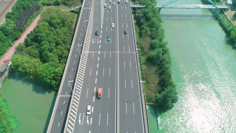 Aerial view of a highway overpass multilevel junction with fast moving cars surrounded by green trees and with a river on a side on a sunny day
