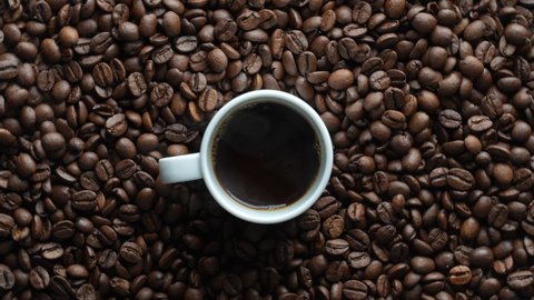 White cup of hot black coffee with a rotating background of fresh roasted coffee beans, close-up, top view. 360 degree rotation. Loop motion