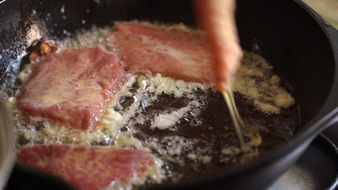Meat chops in batter are placed in hot frying pan. Meat is fried in oil. 