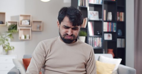 Close up of young Arab tired and sad man working at laptop and getting bad news or result in job. At home. Upset male freelancer at computer. Gamer loosing in game online. Lockdown concept. Lost money