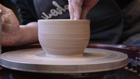 Slow motion video of unrecognizable pottery woman working with pottery wheel in cozy workshop making vase or mug, creative people