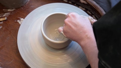 Slow motion video of unrecognizable pottery woman working with pottery wheel in cozy workshop making vase or mug, creative people. Top view