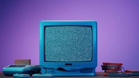 Old television with grey interference screen on purple neon background. Close-up of vintage tv and cartridges for retro playstation. Antique video game, nostalgia. 