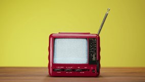 Small old television with grey interference screen on yellow background. Close-up of vintage tv on table, nostalgia. Gray noise screen and glitches.