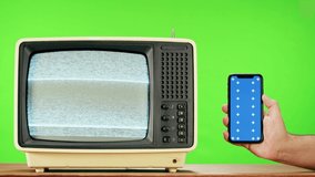 Old television with grey interference screen on green background and smartphone with blue chroma key. Close-up of vintage tv, nostalgia. Gray noise screen and glitches.