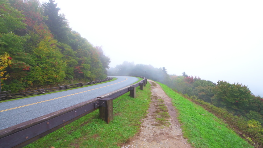 Point of view pov walking handheld shot of traffic car vehicle guard rail barrier at Blue Ridge Parkway road, North Carolina at fall foliage mountains national park forest fog moody weather