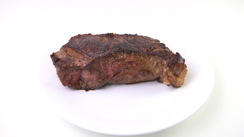Macro closeup of hand turning with tongs cooked roasted or fried new york strip steak cut on white plate on table isolated against white background