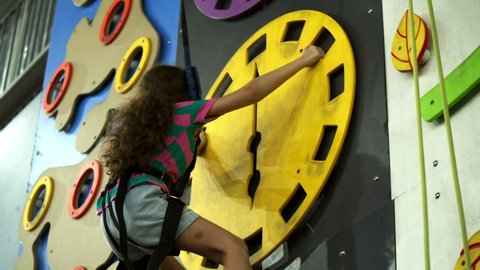 Child is training on the climbing wall. Children's rock climbing in a private school. Climbing exercises. School-age girl climbs the wall of a climbing wall.