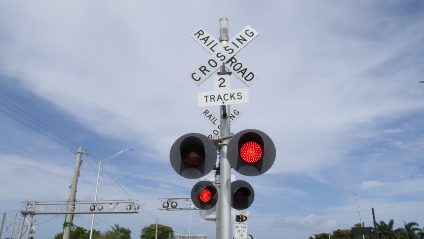 Left and right alternating flashing red lights beneath railroad crossing sign on Sample Road in Pompano Beach, Florida with the Tri-Rail passing by in the background Royalty-Free Stock Footage #1089386549