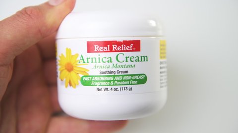 Naples, USA - December 8, 2021: Macro closeup hand holding Real relief arnica montana soothing cream herbal medicinal plant treatment for joint muscle pain relief on isolated white background