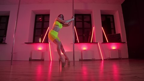 Slim girl near dance pole. Pretty woman doing poledance in studio. Exotic dance at red light background. Exotic dance. Young woman performing sensual pole dance. 4K, UHD