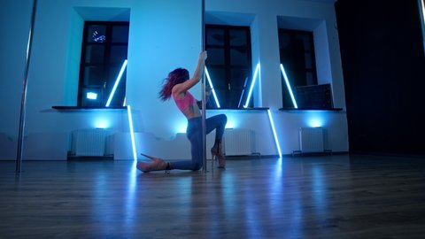 Elegant woman dancing near pole with blue light at background. Dance and acrobatics concept. Sexy female pole dancing on blue background. 4K, UHD