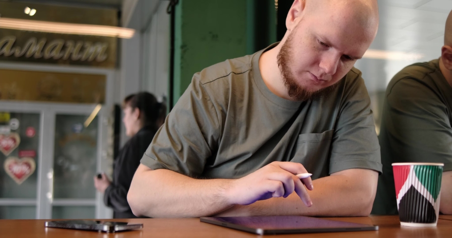 Young creative web designer in casualwear having coffee with cookies and drawing with stylus on tablet while working over