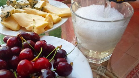 4K resolution video, white sparkling wine poured into a glass at home, shooting surrounded by plates of cherries, cheese and vegetables.