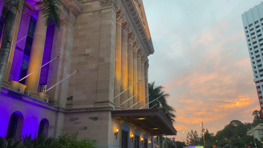Orange Sunset Pan view of Brisbane City Town Hall Clocktower with Purple Lights Illuminating the Palm Trees