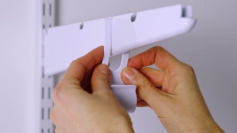Installation brackets of a metal mesh shelf in the dressing room system on a bracket. Hands is assembling a white holder storage system close-up