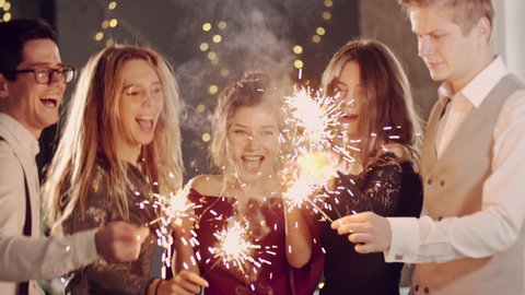 Asian girl and group young college student friends lit light sparkler in hand fireworks, sing and dance together. Woman on Party with people, love friendship relationship and celebration concept.