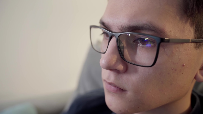 The laptop monitor reflected on the glasses of a young man. Close-up of a focused young businessman. The guy wears computer glasses to reduce eye strain. Royalty-Free Stock Footage #1089398233
