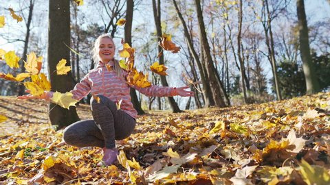 A girl in a city park tosses autumn leaves into the air.