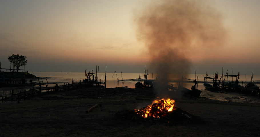 Blurred 4K video background of the morning sun rising from the horizon, bonfires on the beach, for a clean and comfortable morning in a community lifestyle.