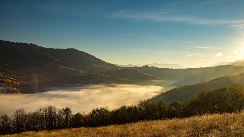 Sunset in highland with big forestry mountains and evening fog fills valley among hill slopes in autumn under orange sky 4K time-lapse video