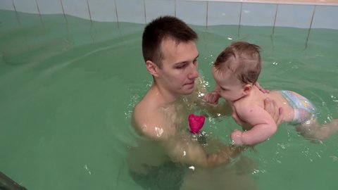 Baby boy is learning to swim with his father in a swimming pool. 