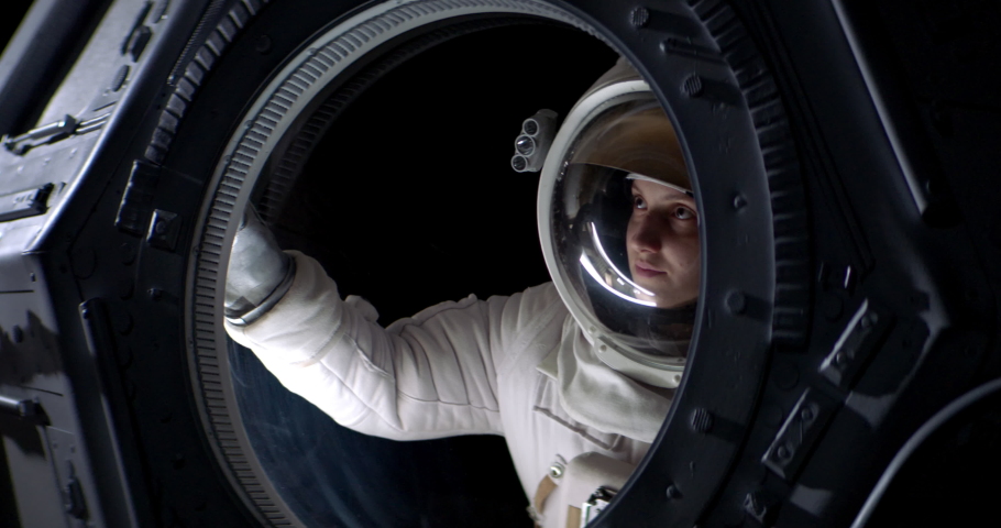 Portrait of Caucasian female astronaut flying towards spaceship cupola window. Space exploration, Mars mission. Shot with 2x anamorphic lens