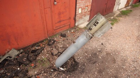 Closeup view 4k stock video footage of real unexploded military missile, torpedo or shell stuck in ground near doors of garages outdoors. Moments of dreadful war of Russia against Ukraine in 2022