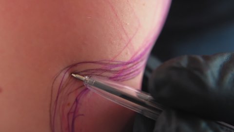 Tattoo artist girl at work. A feminist with dreadlocks gets a tattoo. A strong woman gets a tattoo. Close-up. Slow motion. the master draws a sketch on the model's hand. LGBTQ+