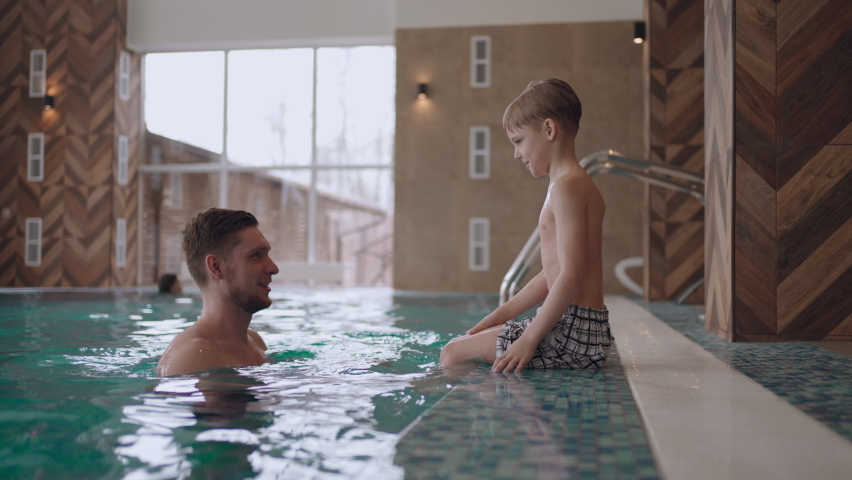 father is teaching son to swim in swimming pool of modern wellness spa, healthy lifestyle