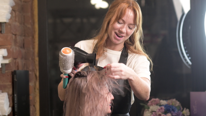 Hairdresser in studio dries hair of female customer with hairdryer. professional stylist creates hairstyle in salon. master takes care of client's hair. Royalty-Free Stock Footage #1089407781