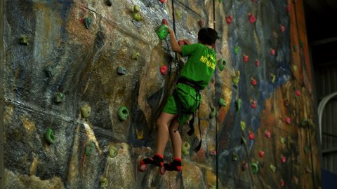 Child is training on the climbing wall with an instructor. Children's rock climbing in a private school. Climbing exercises. School-age boy climbs the wall climbing wall.Saigon, Vietnam, April 6, 2022