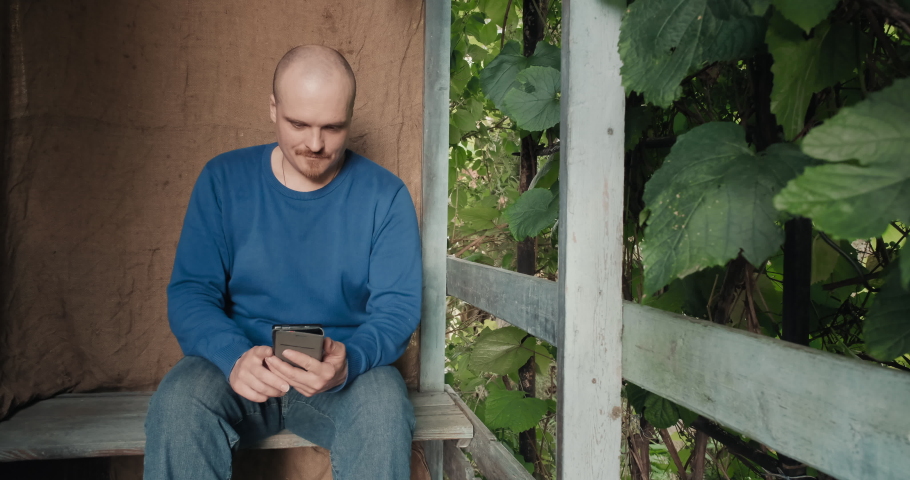 Man is sitting on the porch of a village house and reading an electronic. The concept of reading electronic books, studying and hobbies. Old, retro decor, burlap background