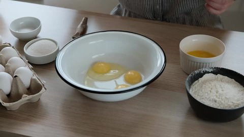 Woman adding sugar in a bowl with eggs to beat the dough. The process of making dough for buns with ingredients on a table.