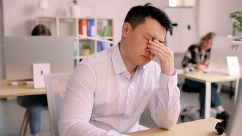 Boring asian businessman trying to work at coworking. Bored office worker tired during working with colleagues in the office.