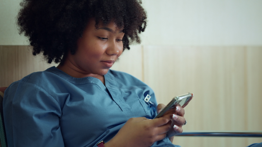 Happy African American female nurse dressed in scrubs using smartphone apps texting message to remote patient at hospital, Practice of medicine and public health care supported by mobile concept. Royalty-Free Stock Footage #1089415683