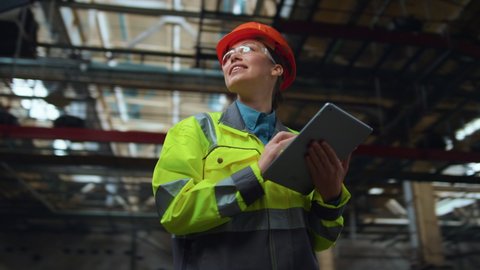 Стоковое видео: Supervisor woman analysing work at modern manufacturing production warehouse. Brunette industrial engineer holding digital technologies tablet computer at storage. Serious factory work concept.