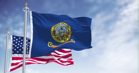The Idaho state flag waving along with the national flag of the United States of America. In the background there is a clear sky. Idaho is a state in the Pacific Northwest region of the United States