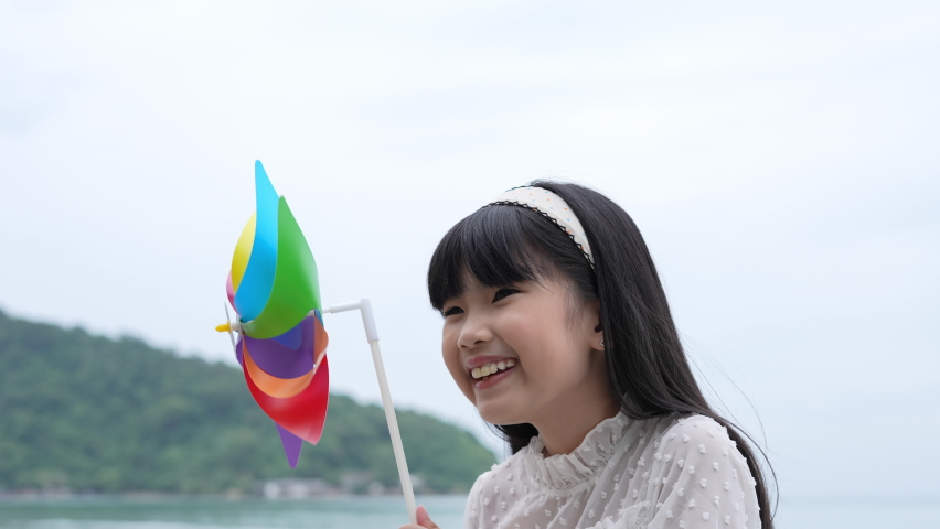 Holiday concept of 4k Resolution. Asian girl smiling happily on the beach. children playing with windmills. summer vacation travel.