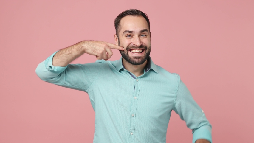 Happy excited confident vivid young brunet man 20s wears blue shirt looking camera showing pointing at his smile mouth isolated on plain plain pink background studio. People emotions lifestyle concept Royalty-Free Stock Footage #1089417519