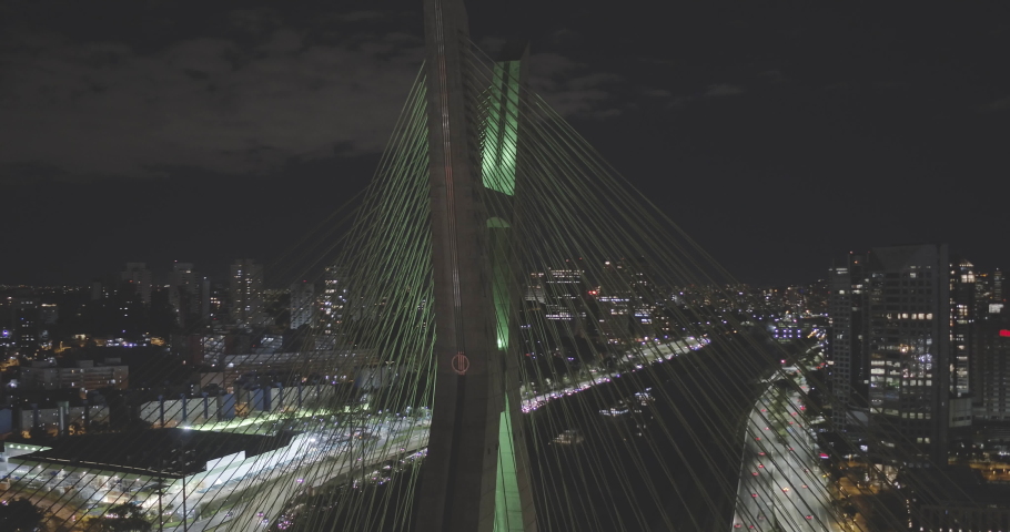 Aerial footage going around estaiada bridge with green light at night in Sao Paulo with heavy traffic