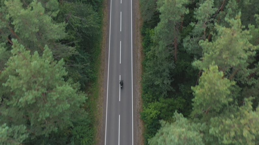 Aerial shot to biker riding on motorbike through forest road. Motorcyclist racing his motorcycle on country road at green wood. Man drive bike during trip. Concept of freedom and adventure. Top view Royalty-Free Stock Footage #1089418313