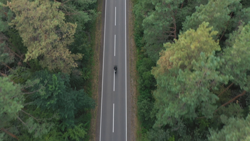 Aerial shot to biker riding on motorbike through forest road. Motorcyclist racing his motorcycle on country road at green wood. Man drive bike during trip. Concept of freedom and adventure. Top view | Shutterstock HD Video #1089418313