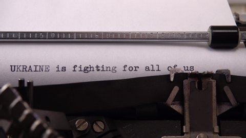 Typing phrase "UKRAINE is fighting for all of us" on retro typewriter.