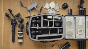 Professional  photographer packs smart backpack with equipment screw the stick into the remote controler. Top view on suitcase with lens camera and drone drone and gimbal